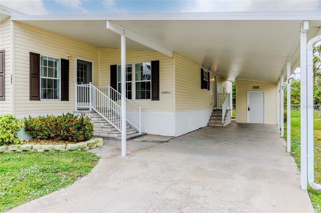 A light yellow manufactured home features a covered carport, white stairs, and dark window shutters — 2100 KINGS HIGHWAY UNIT 390, PORT CHARLOTTE, FL