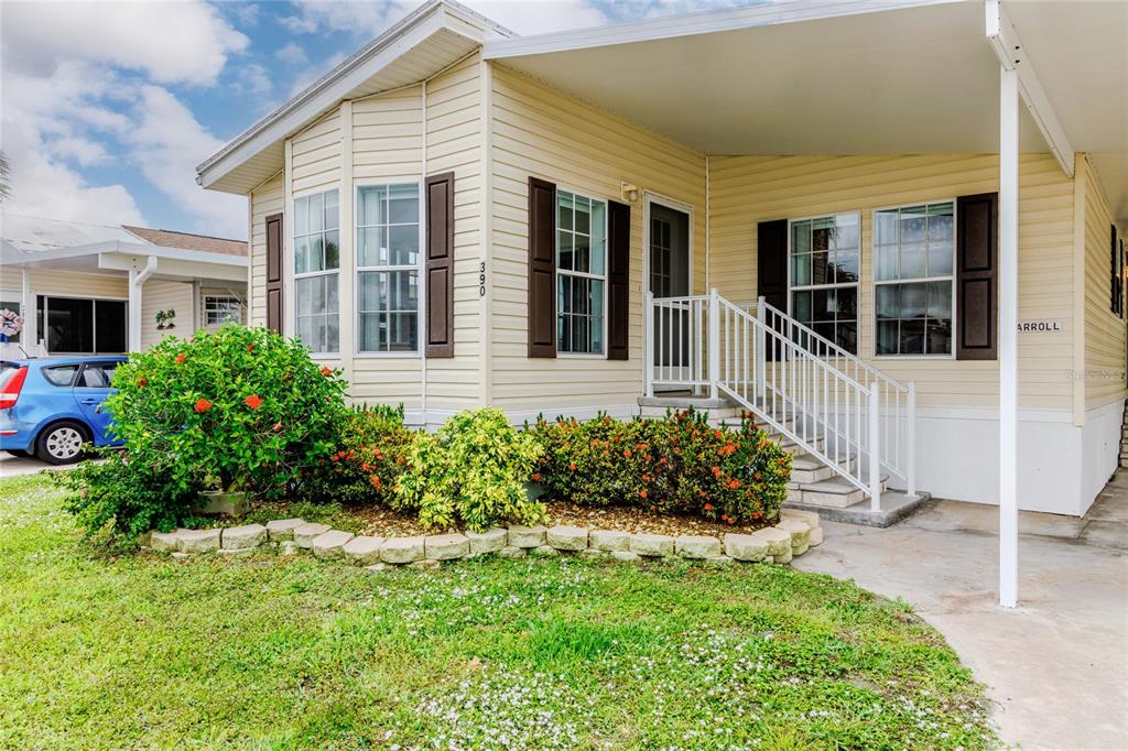 A yellow manufactured home features a front porch, white railings, and a landscaped garden bed — 2100 KINGS HIGHWAY UNIT 390, PORT CHARLOTTE, FL