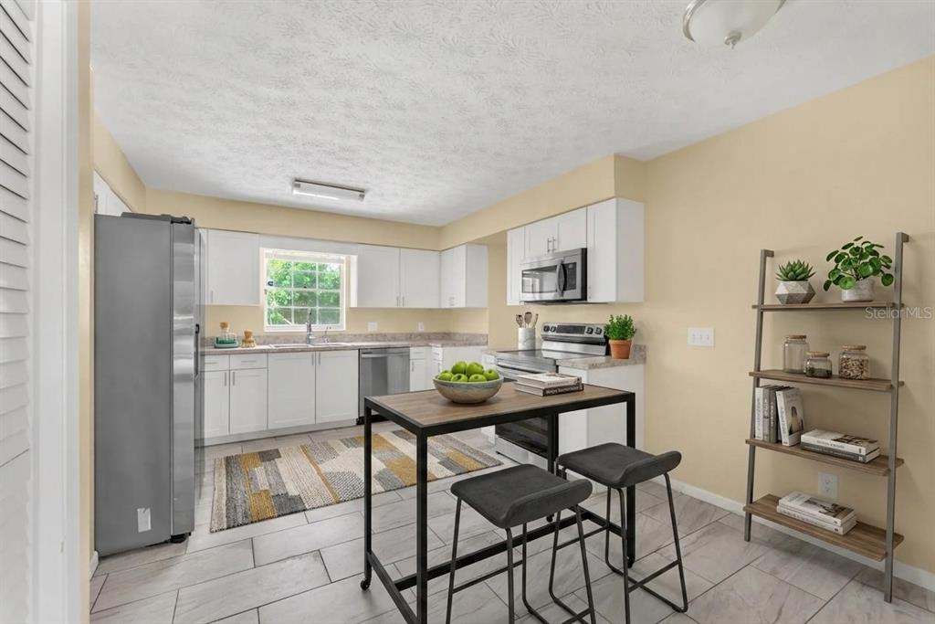 A kitchen features white cabinets, stainless steel appliances, a center island, and light-colored tile flooring — 1909 LIDO DRIVE, BRANDON, FL