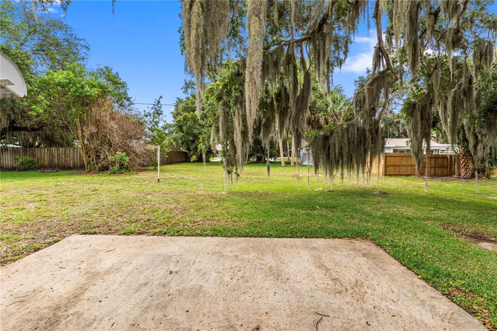 A concrete patio overlooks a grassy backyard shaded by large trees with hanging Spanish moss — 326 BELFAST TERRACE, SEBASTIAN, FL
