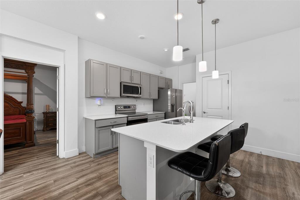 A modern kitchen features gray cabinets, white countertops, a central island, and wood-look flooring — 5465 GAITOR TERRACE, NORTH PORT, FL