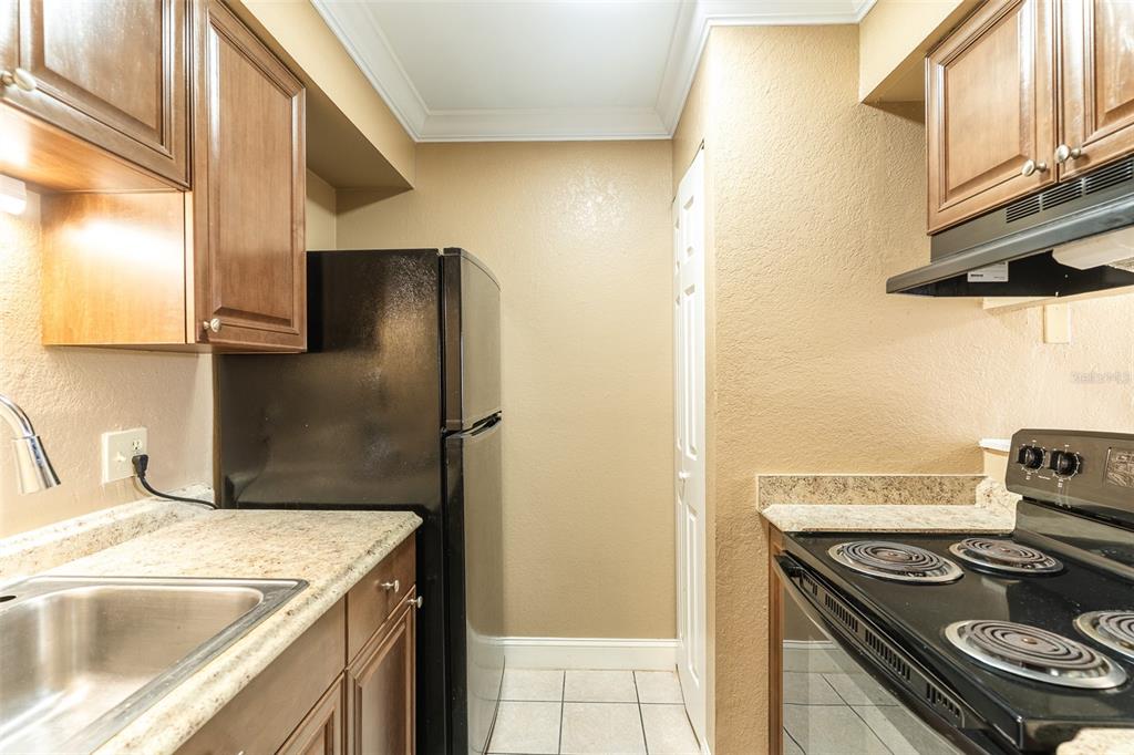 A kitchen features brown cabinets, a black refrigerator, a black stove, and light-colored countertops — 118 OAK CREST DRIVE NW, WINTER HAVEN, FL