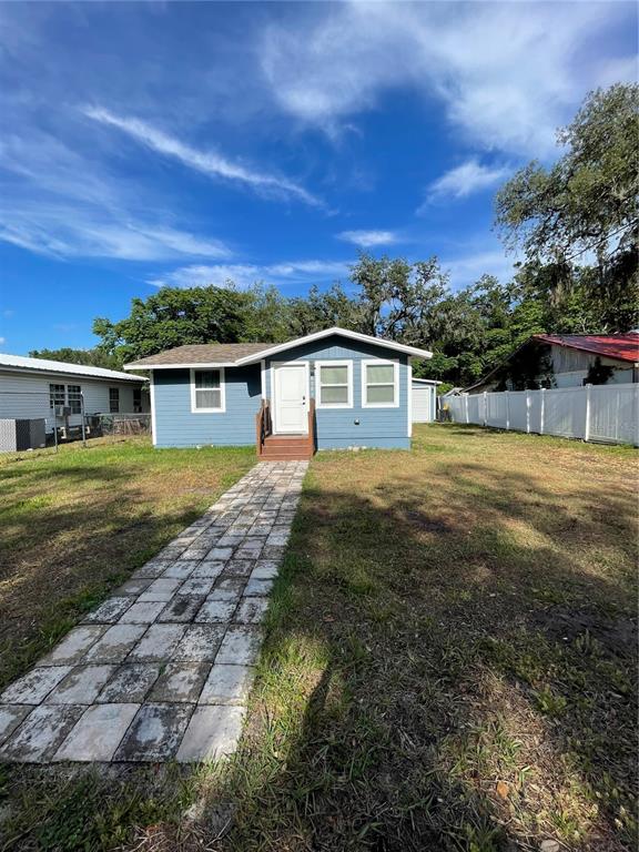 A blue single-story house features a stone walkway leading to a front wooden porch — 4308 PLUM STREET, ZEPHYRHILLS, FL