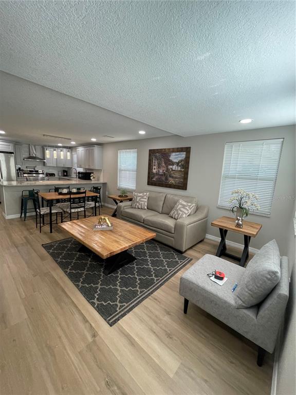 An open-concept living room and kitchen featuring light wood flooring and neutral-toned furniture — 4308 PLUM STREET, ZEPHYRHILLS, FL