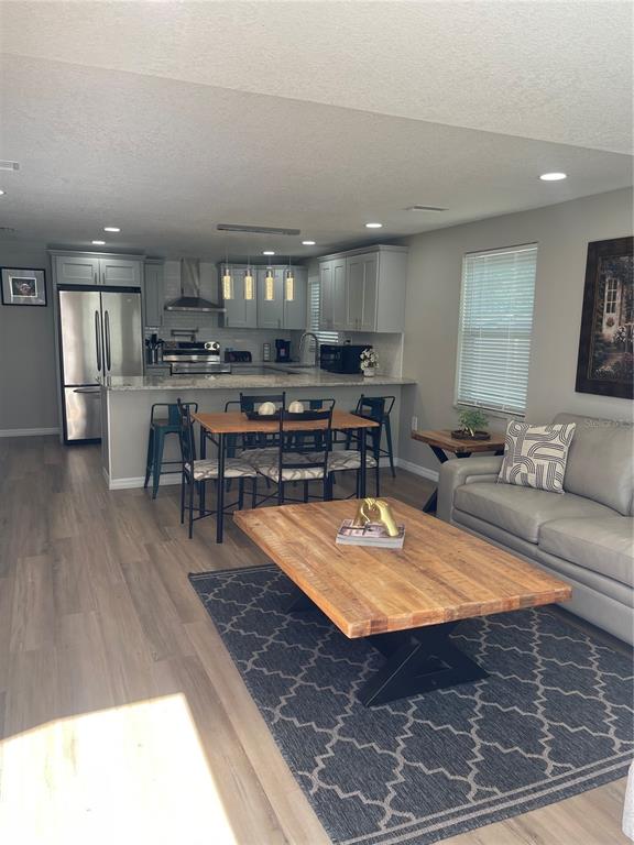 An open-concept kitchen and living area featuring light gray cabinets, wood flooring, and a dining table — 4308 PLUM STREET, ZEPHYRHILLS, FL