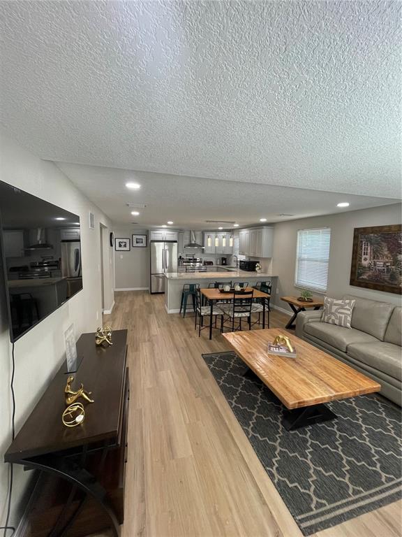 An open-concept living room and kitchen feature light wood flooring and a large wooden table — 4308 PLUM STREET, ZEPHYRHILLS, FL