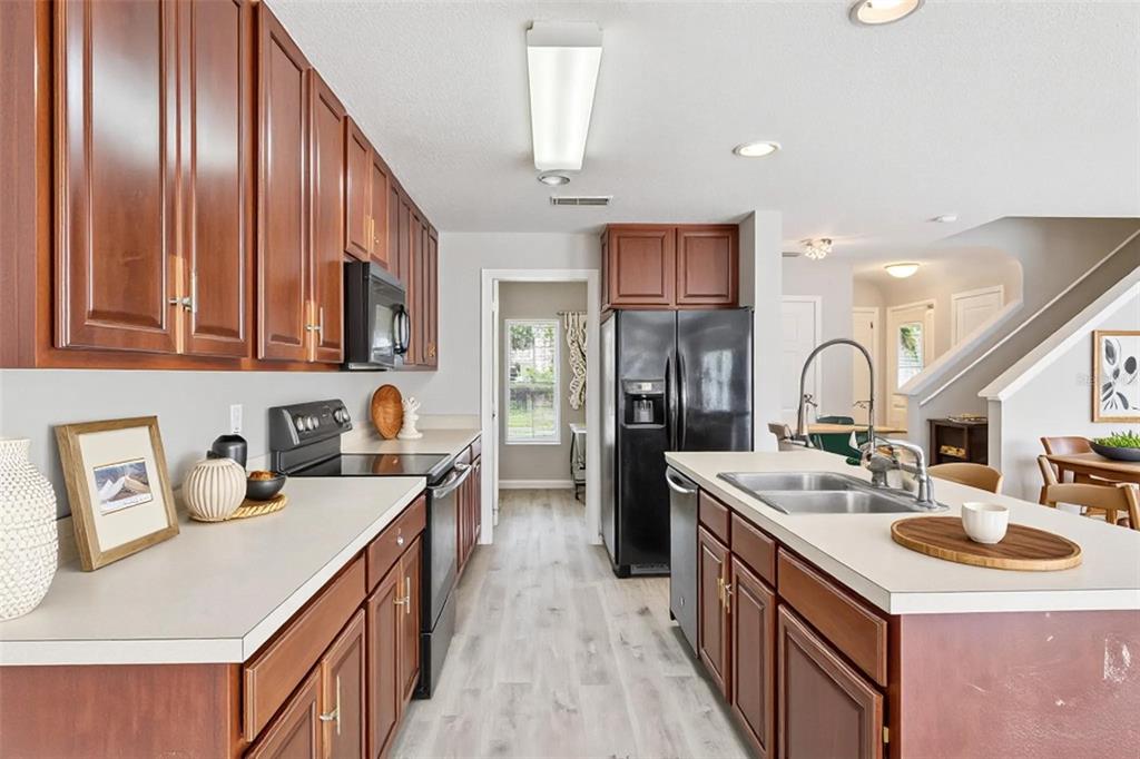 A kitchen features wood cabinets, black appliances, a central island, and light-colored countertops — 3026 WILD TAMARIND BOULEVARD UNIT 3026, ORLANDO, FL