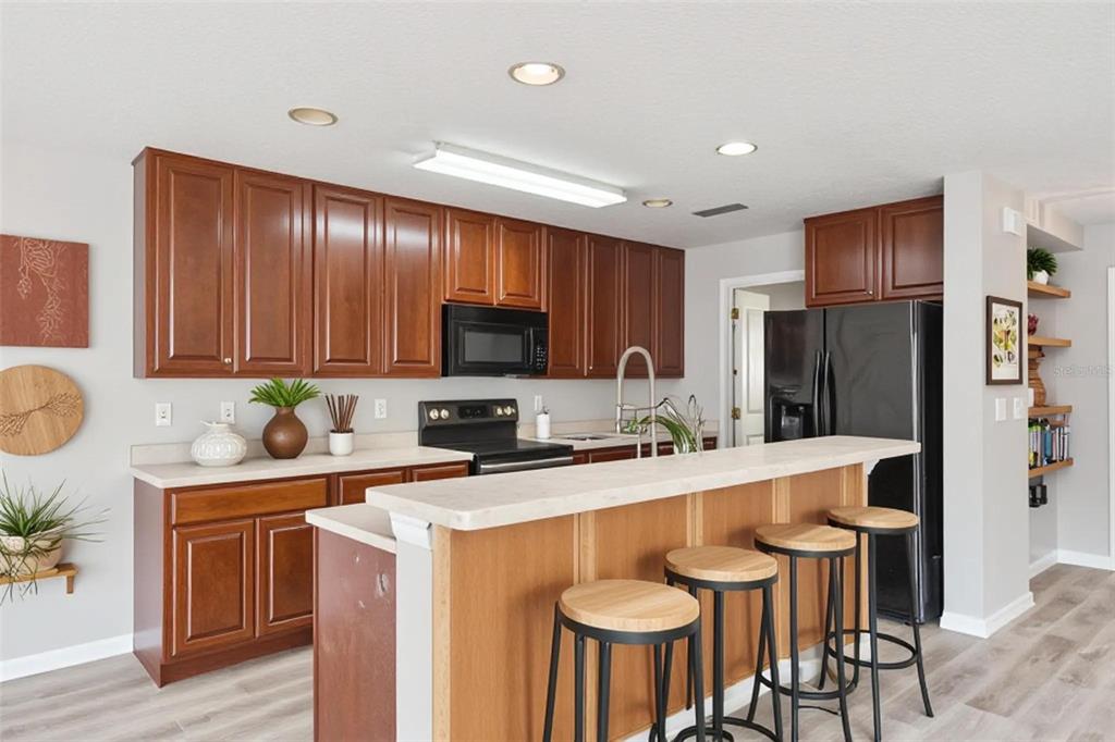 A kitchen features wood cabinets, black appliances, a breakfast bar with stools, and light flooring — 3026 WILD TAMARIND BOULEVARD UNIT 3026, ORLANDO, FL