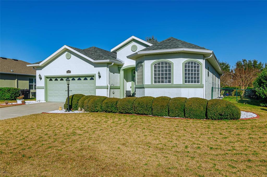 A single-story house with a green garage door, arched windows, and a manicured hedge — 6369 SW 89TH LOOP, OCALA, FL