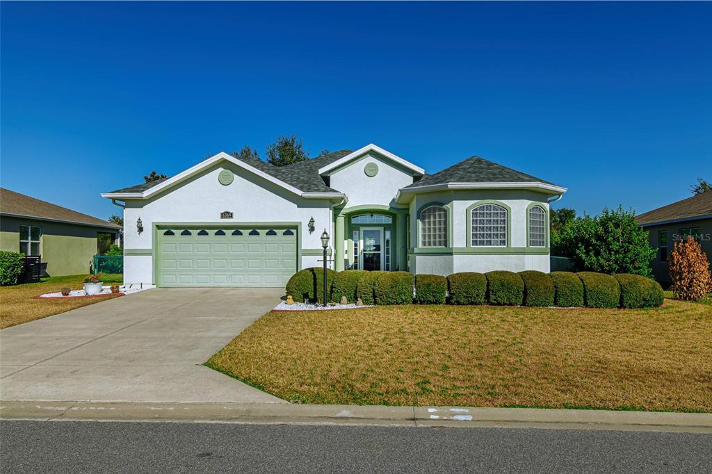 A single-story house with a green garage door, stucco exterior, and a manicured hedge — 6369 SW 89TH LOOP, OCALA, FL