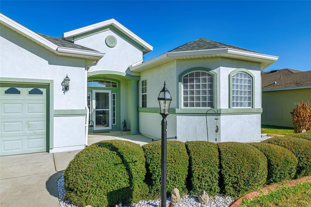 The exterior of a single-story home features a light-colored stucco facade, green trim, and landscaping — 6369 SW 89TH LOOP, OCALA, FL