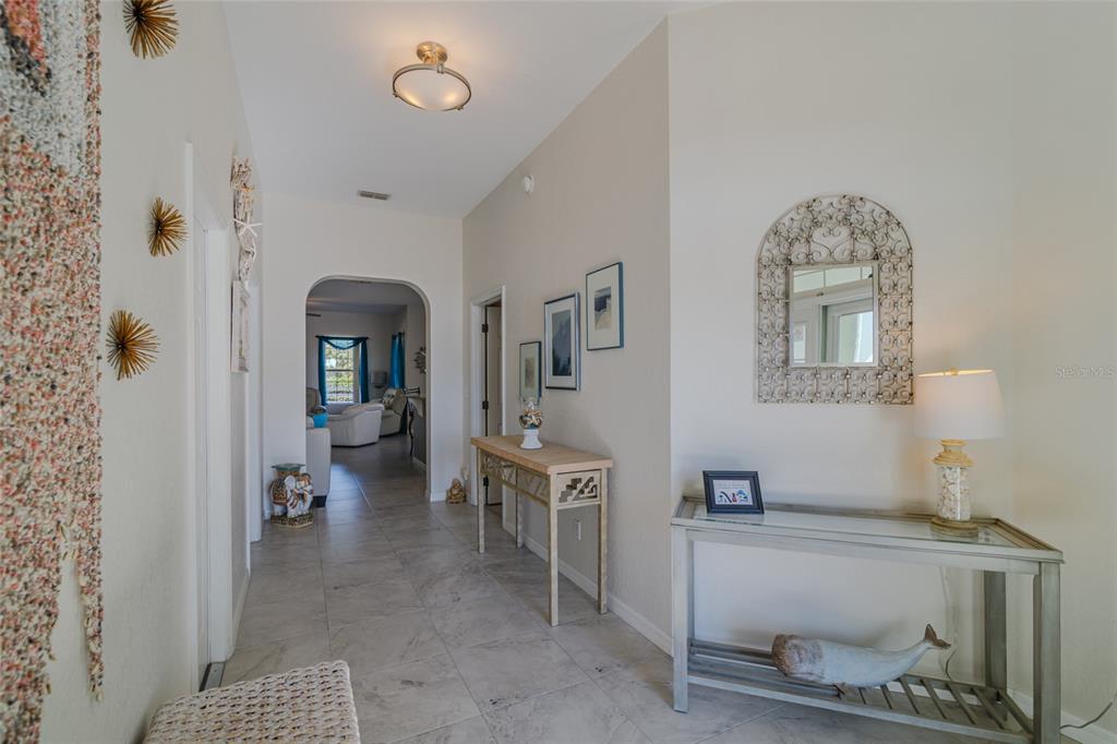 A bright entryway features tiled floors, two console tables, wall art, and an arched doorway — 6369 SW 89TH LOOP, OCALA, FL