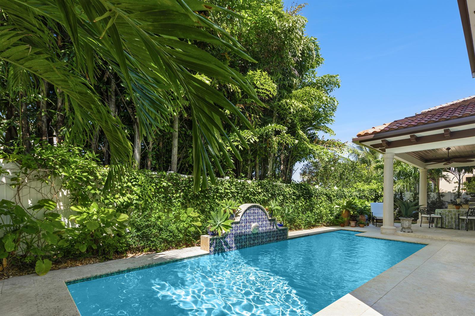A rectangular swimming pool with a tiled fountain feature sits beside a covered patio area — 229 Edmor Road, West Palm Beach FL 33405, WEST PALM BEACH, FL