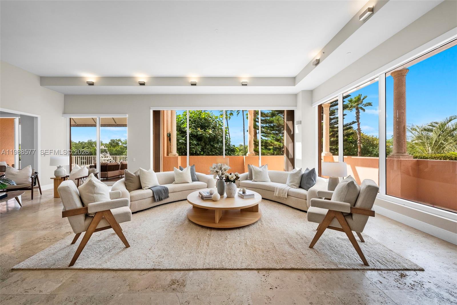 A bright living room features curved sofas, a round coffee table, and large glass windows — 10 Edgewater Dr, Coral Gables FL 33133, CORAL GABLES, FL