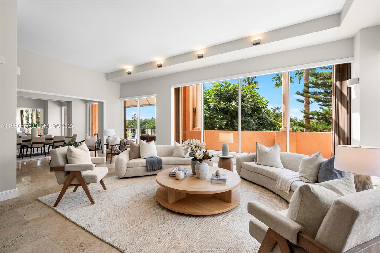 A bright living room features curved sofas, a round wooden coffee table, and large windows — 10 Edgewater Dr, Coral Gables FL 33133, CORAL GABLES, FL