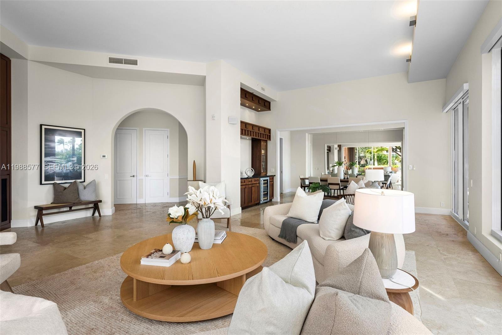 A living room features a round wooden coffee table, neutral sofas, and a built-in bar — 10 Edgewater Dr, Coral Gables FL 33133, CORAL GABLES, FL