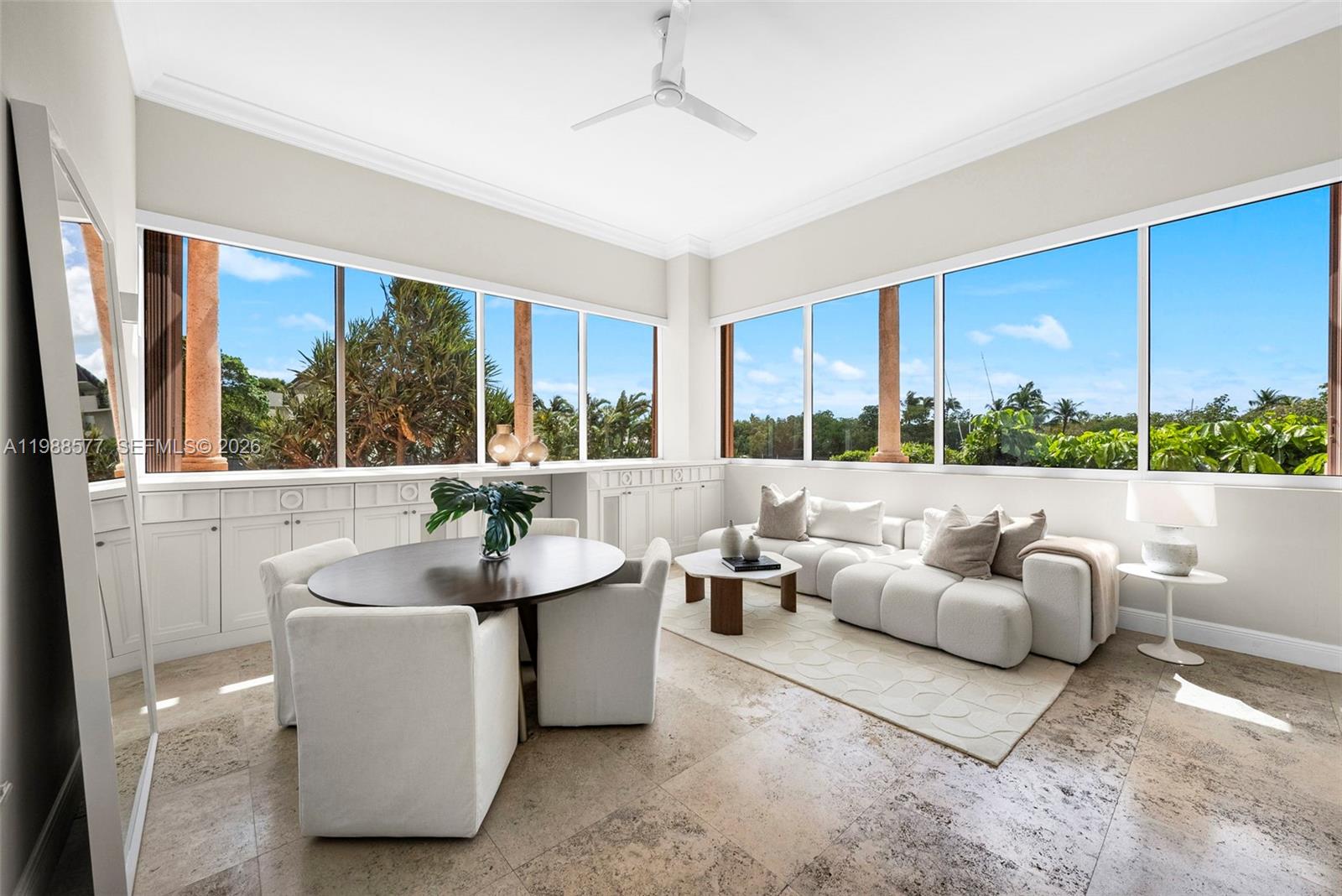 A bright living and dining area features large windows, white cabinetry, and stone flooring — 10 Edgewater Dr, Coral Gables FL 33133, CORAL GABLES, FL