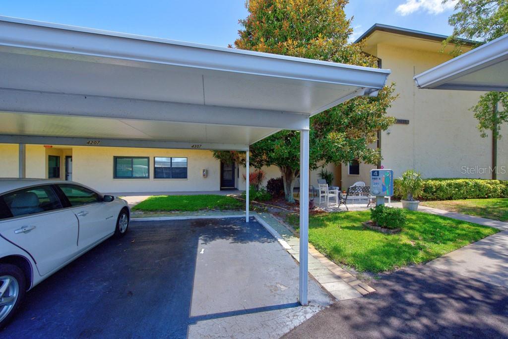 A covered parking space sits in front of a multi-story apartment building with outdoor seating — 12300 VONN ROAD UNIT 4307, LARGO, FL