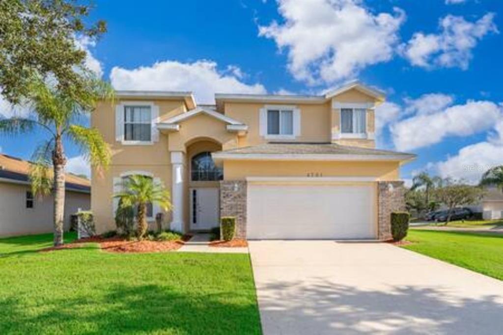 A two-story suburban house with a beige stucco exterior, a two-car garage, and a lawn — 4701 RUBY RED LANE, KISSIMMEE, FL