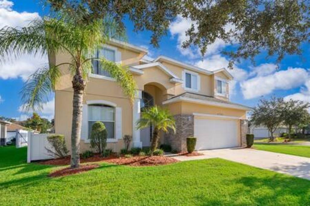 A two-story suburban house with a tan stucco exterior, a two-car garage, and palm trees — 4701 RUBY RED LANE, KISSIMMEE, FL