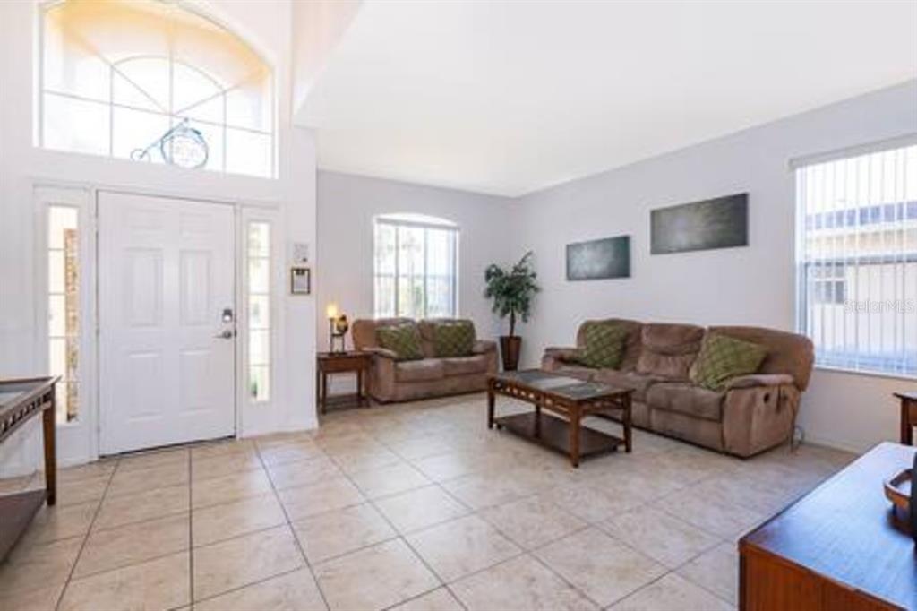 A living room with tile flooring, two brown sofas, a coffee table, and a front door — 4701 RUBY RED LANE, KISSIMMEE, FL