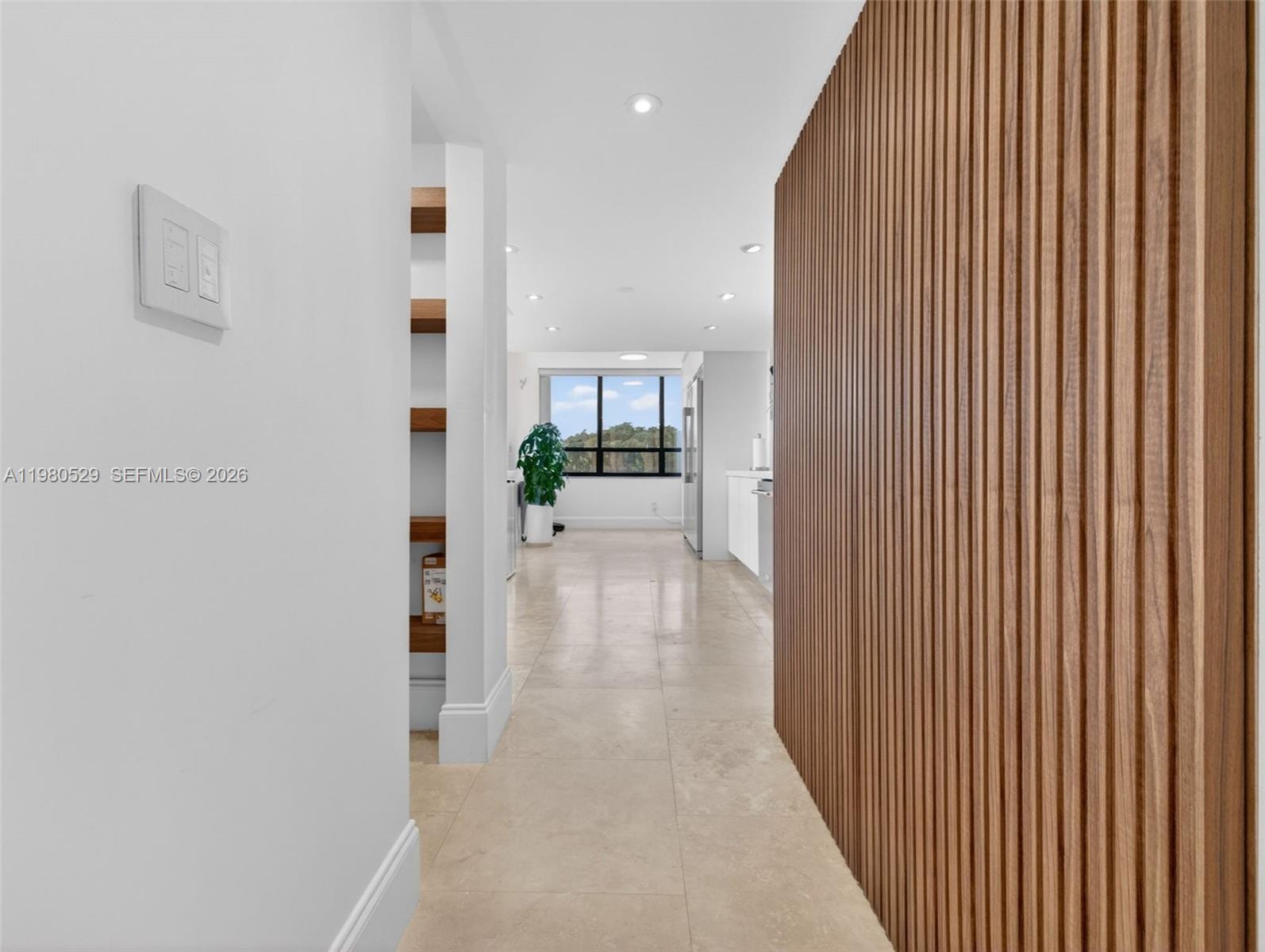 A hallway with light tile flooring leads to a kitchen featuring a wood-slatted accent wall — 11113 Biscayne Blvd # 351, Miami FL 33181, MIAMI, FL