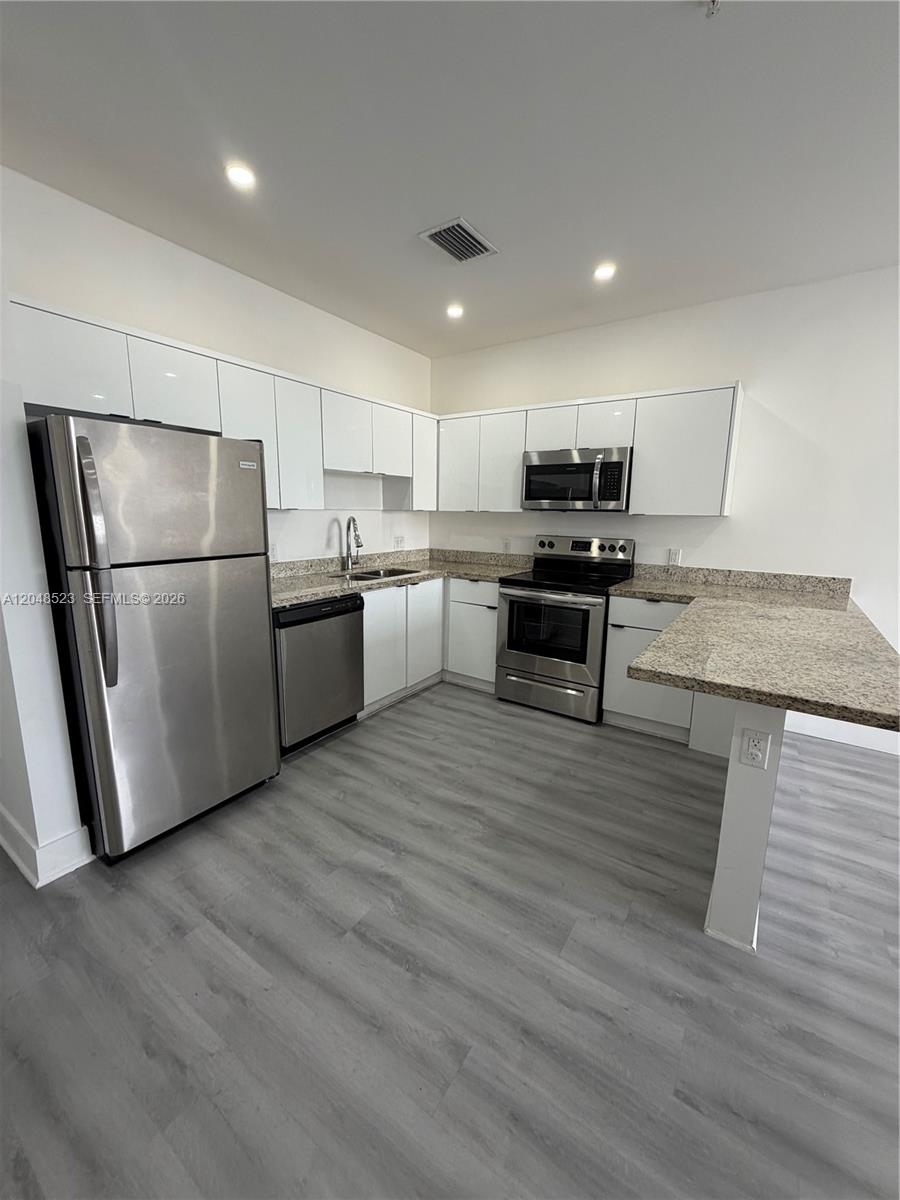 A kitchen features white flat-panel cabinets, stainless steel appliances, and speckled granite countertops — 853 E 24th St # 403, Hialeah FL 33013, HIALEAH, FL
