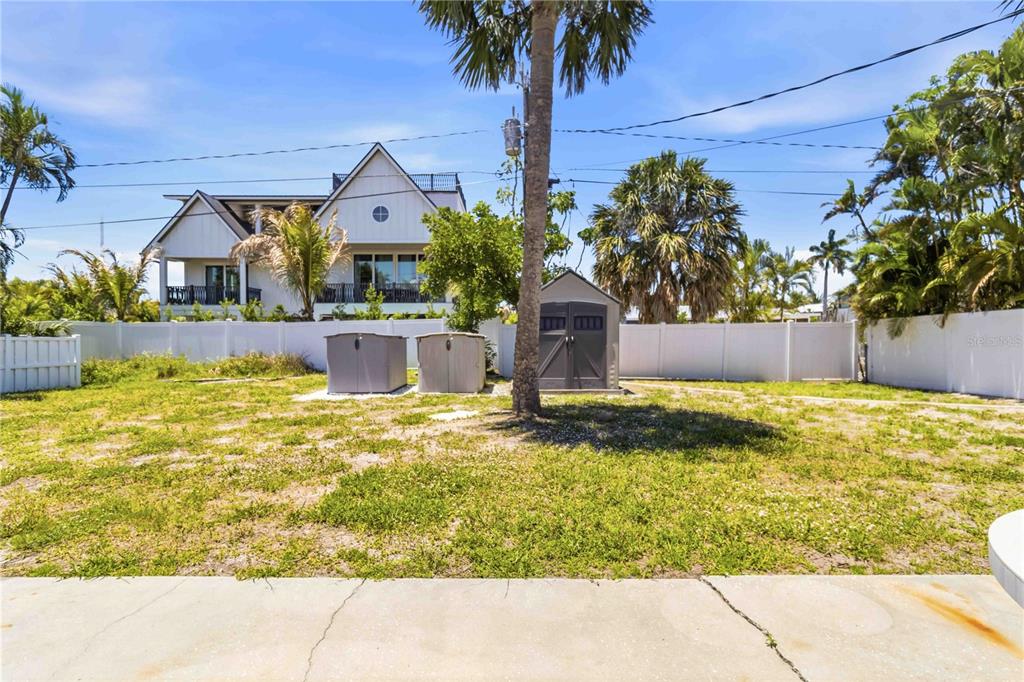 A backyard features a grassy lawn, a storage shed, two utility bins, and a white fence — 306 PALM AVENUE, ANNA MARIA, FL