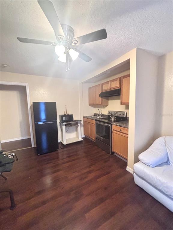 A kitchen with wood cabinets, stainless steel appliances, and dark flooring opens to a living area — 1513 N CENTRAL AVENUE, KISSIMMEE, FL