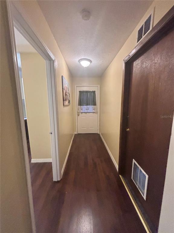 A hallway with wood-look flooring leads to a white door with a curtained window — 1513 N CENTRAL AVENUE, KISSIMMEE, FL