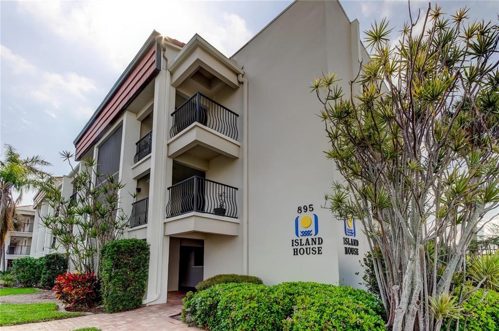 A three-story apartment building exterior with balconies and landscaping under a bright sky — 895 S GULFVIEW BOULEVARD UNIT 303, CLEARWATER BEACH, FL