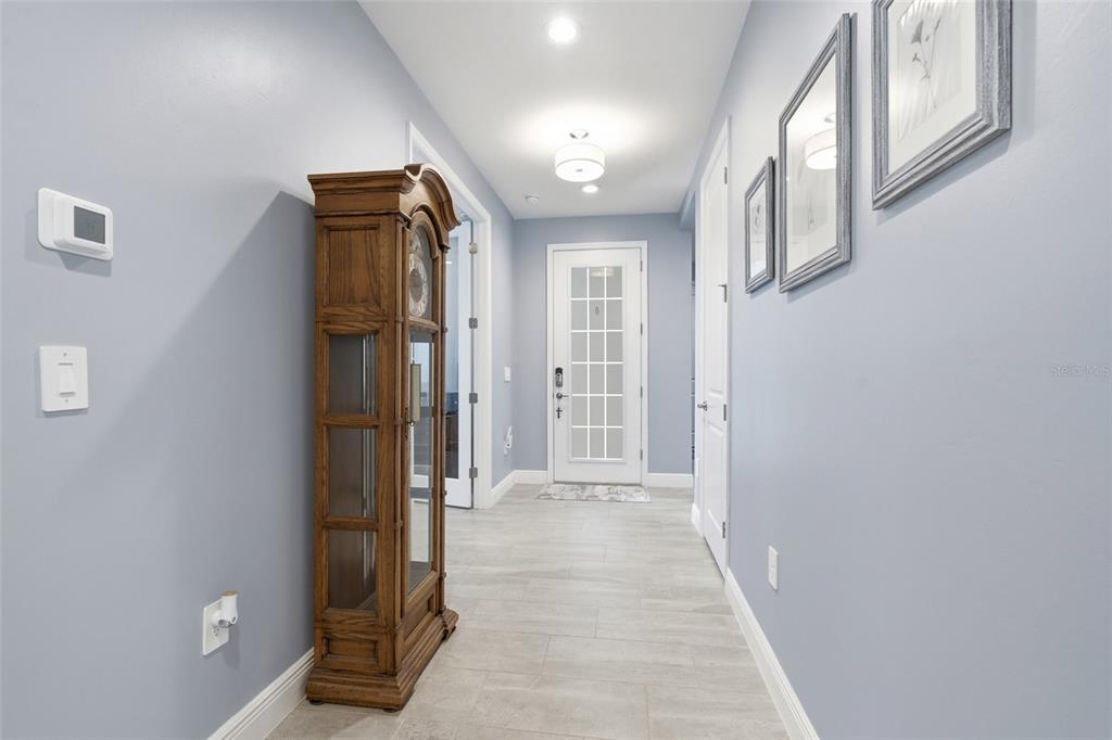 A hallway with light blue walls, tile flooring, a grandfather clock, and a glass-paneled door — 3121 HERITAGE PINES DRIVE, FORT MYERS, FL