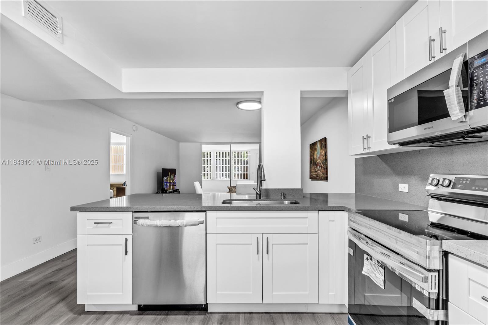 A modern kitchen features white cabinets, stainless steel appliances, and a gray countertop — 445 NE 195th St # 125, Miami FL 33179, MIAMI, FL