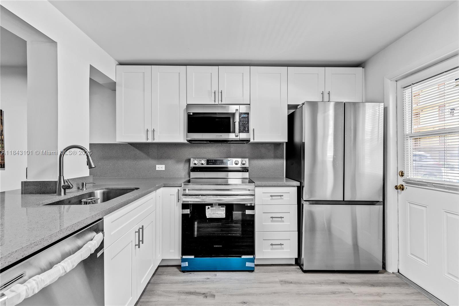 A kitchen features white cabinets, stainless steel appliances, and gray countertops — 445 NE 195th St # 125, Miami FL 33179, MIAMI, FL