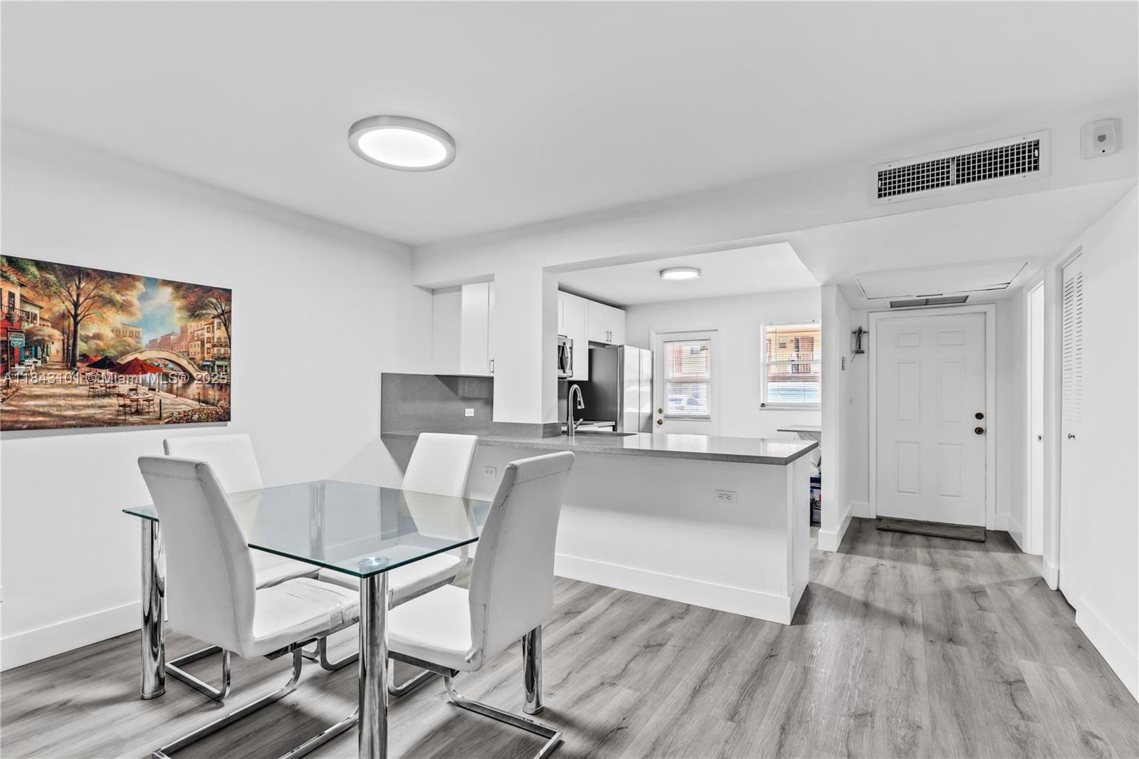 A dining area with a glass table and white chairs sits adjacent to a kitchen — 445 NE 195th St # 125, Miami FL 33179, MIAMI, FL