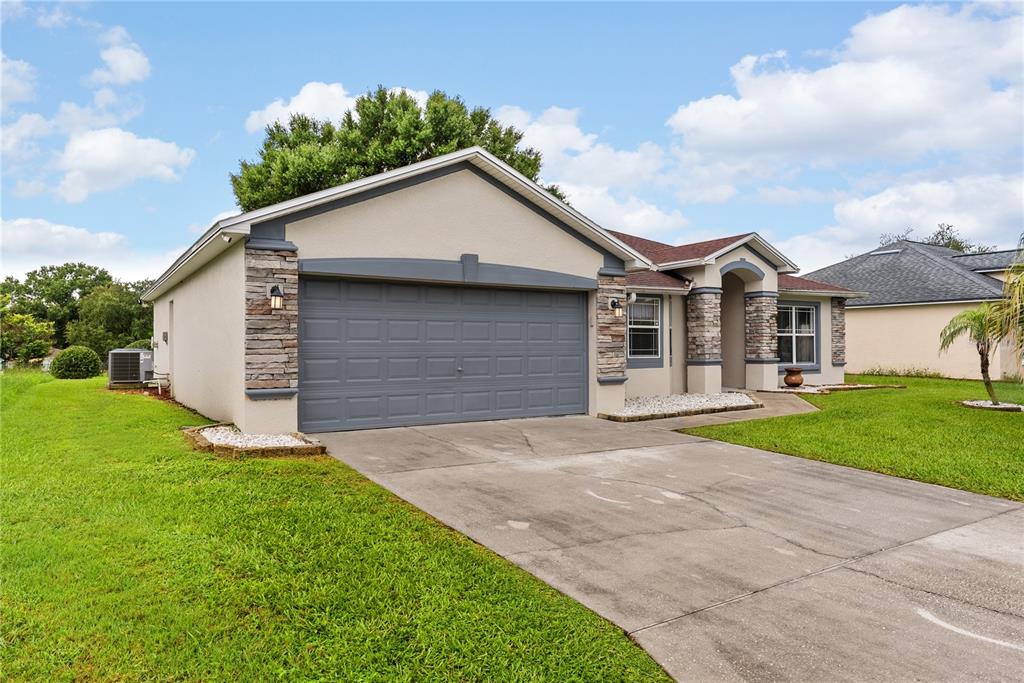 A single-story house with a gray garage door, stone accents, and a concrete driveway — 8207 WESTMONT TERRACE DRIVE, LAKELAND, FL