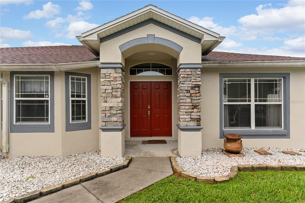 The exterior of a house features a red double front door and stone-accented columns — 8207 WESTMONT TERRACE DRIVE, LAKELAND, FL