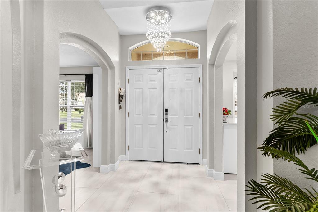 A bright foyer features white tile floors, a crystal chandelier, and double front entry doors — 8207 WESTMONT TERRACE DRIVE, LAKELAND, FL