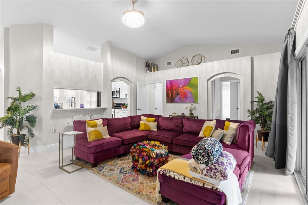 A living room features a large purple sectional sofa, a colorful rug, and high ceilings — 8207 WESTMONT TERRACE DRIVE, LAKELAND, FL