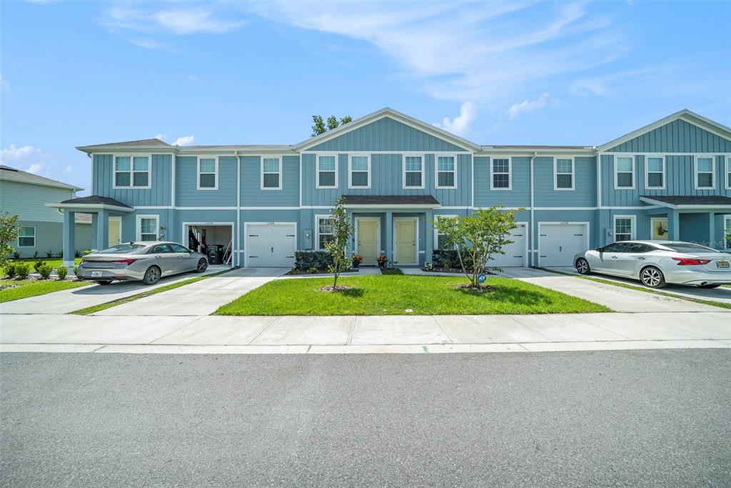 A row of blue two-story townhomes with attached garages and driveways under a blue sky — 12264 GRIZZLY LANE, NEW PORT RICHEY, FL