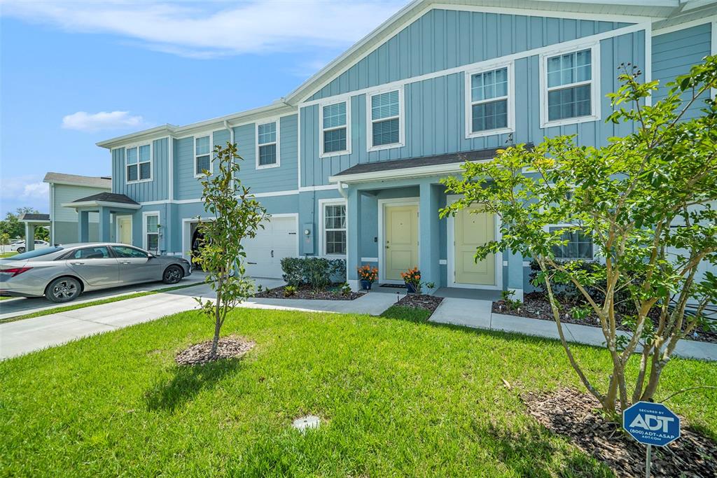 A blue two-story townhouse with a white garage and two front doors sits on grass — 12264 GRIZZLY LANE, NEW PORT RICHEY, FL