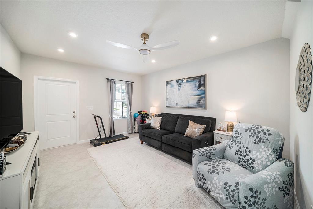 A living room features a dark sofa, a patterned armchair, a treadmill, and tile flooring — 12264 GRIZZLY LANE, NEW PORT RICHEY, FL