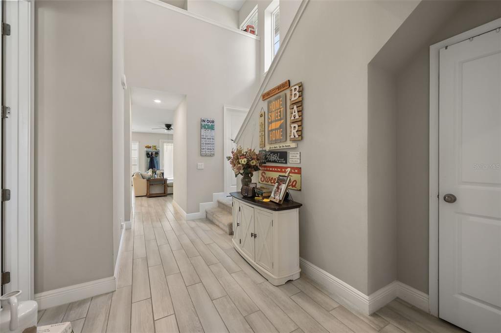 A foyer features light wood-look tile flooring, a white console table, and a staircase wall — 7805 NEMOURS PARKWAY, ORLANDO, FL