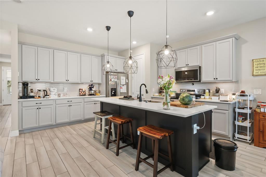 A kitchen features light gray cabinets, a dark island with bar stools, and pendant lighting — 7805 NEMOURS PARKWAY, ORLANDO, FL