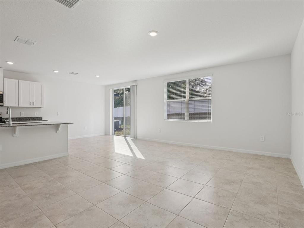 A bright, open-concept living and dining area features white walls, tile flooring, and a kitchen — 2896 WILD OLIVE DRIVE, ST CLOUD, FL