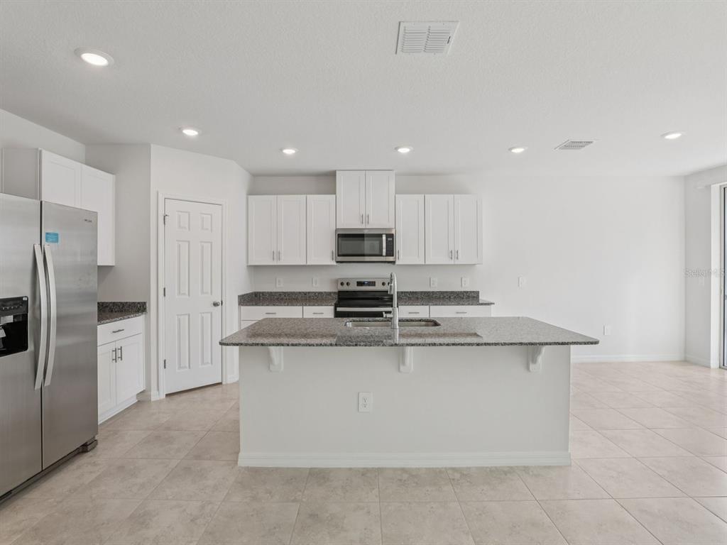 A kitchen features white cabinetry, granite countertops, a central island, and stainless steel appliances — 2896 WILD OLIVE DRIVE, ST CLOUD, FL
