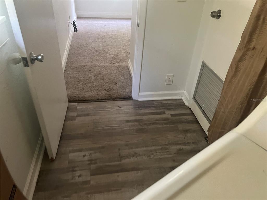A bathroom with wood-look flooring leads into a carpeted bedroom through an open doorway — 9102 6TH AVENUE, JACKSONVILLE, FL