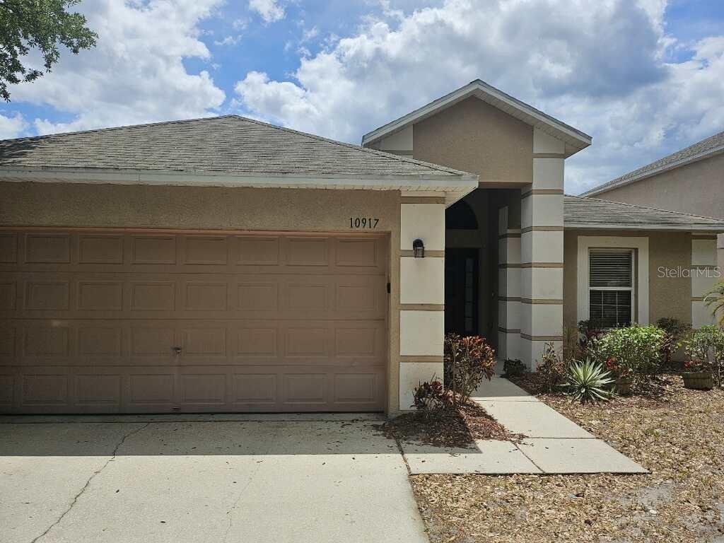A single-story house with a beige stucco exterior, a two-car garage, and a covered entryway — 10917 BANYAN WOOD WAY, RIVERVIEW, FL
