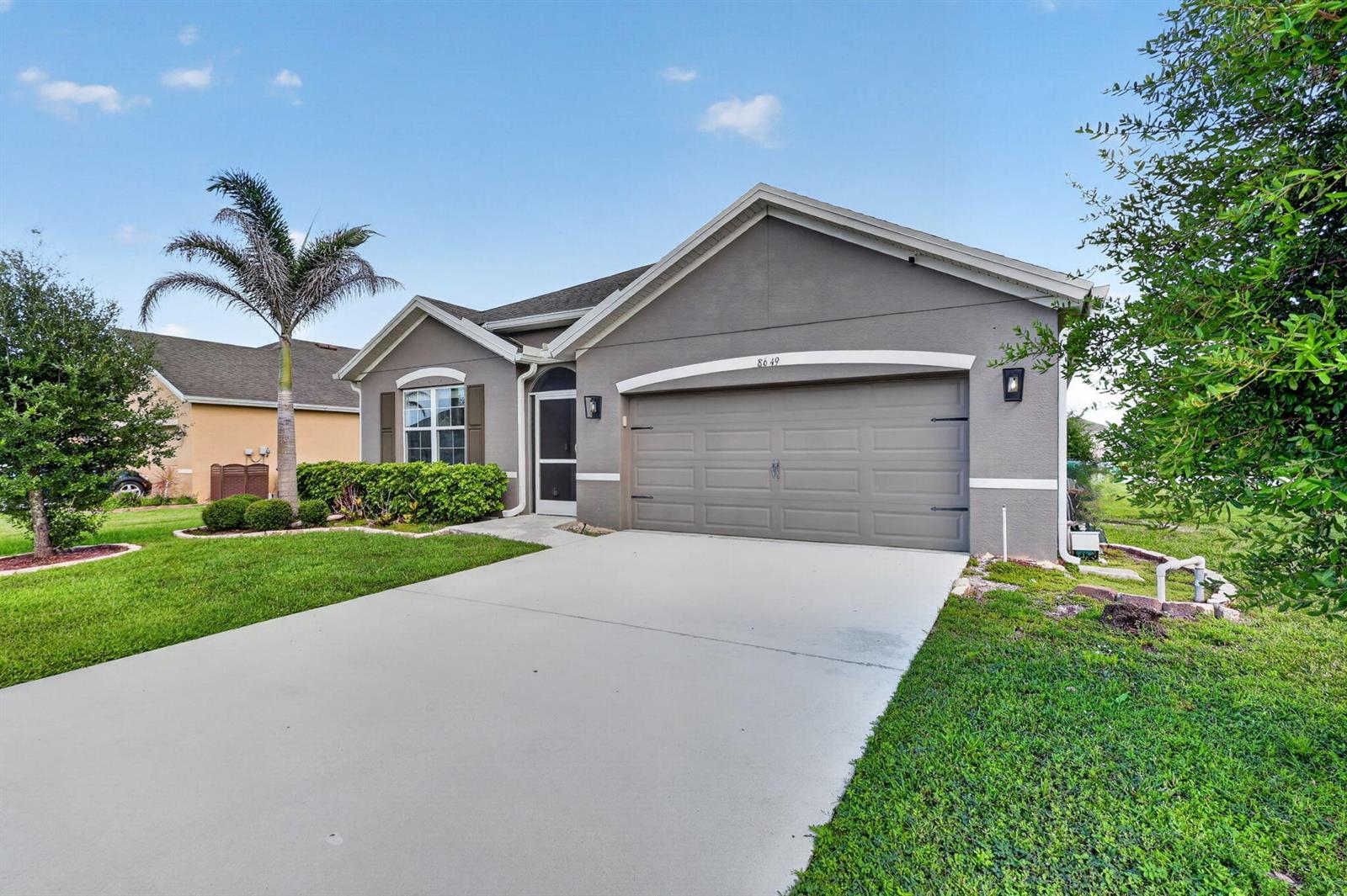 A gray single-story house with a two-car garage, a palm tree, and a concrete driveway — 8649 Cobblestone Drive, Fort Pierce FL 34945, FORT PIERCE, FL