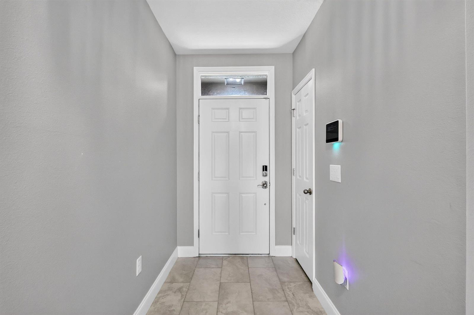 A gray-walled entryway features a white front door, tiled flooring, and a wall-mounted security panel — 8649 Cobblestone Drive, Fort Pierce FL 34945, FORT PIERCE, FL